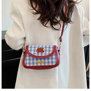 Detail of blue plaid saddle bag with red apple embroidery and slim shoulder strap