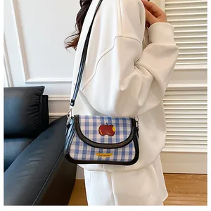 Close-up of blue plaid saddle bag featuring a red apple patch and black leather trim