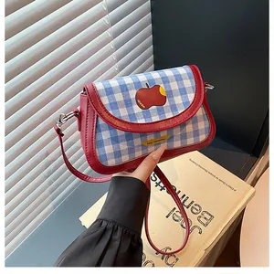 Detail of blue plaid saddle bag featuring red leather trim and apple patch embroidery