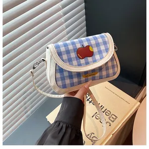 Detail of blue plaid saddle bag with apple patch and slim white shoulder strap