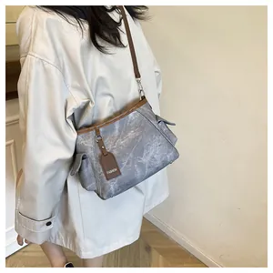 Detail of grey marbled bucket bag with brown leather straps worn by a model in a room