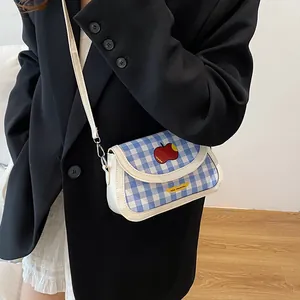 Blue gingham saddle bag with apple patch and thin white shoulder strap shown on model