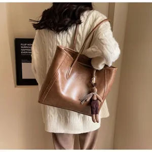 Brown faux leather tote bag with doll pendant styled on a cozy autumn knit sweater