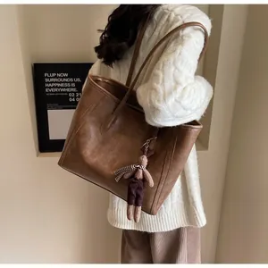 Brown vintage PU leather tote bag with cute bear charm shown on a female model shoulder
