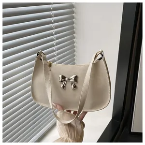 Gros plan d'un sac crème avec une boucle papillon argentée et une fermeture éclair en métal