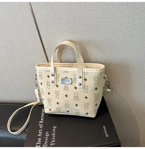 Détail du sac seau crème avec imprimés d'ours et plaque logo en métal argenté brillant