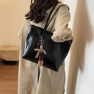 Black glossy leather tote bag with rabbit charm shown on a beige trench coat