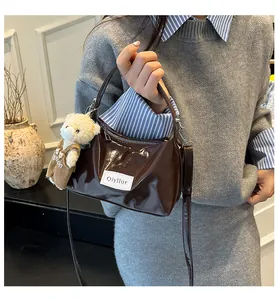 Brown glossy patent leather handbag featuring a white brand label and cute plush bear charm