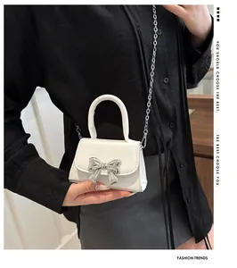 Detail of white mini crossbody bag with silver metal bow and delicate chain strap
