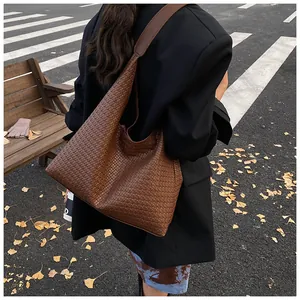 Outdoor street view of a large dark brown woven leather hobo tote bag on shoulder
