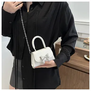 Close-up of white mini square bag with silver bow buckle and chain strap on model