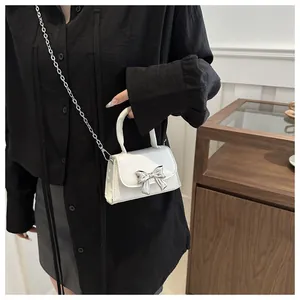 Detail of white leather mini crossbody bag with silver bow accent and metal chain strap