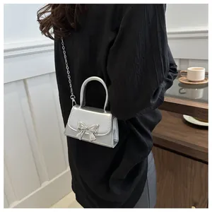 Silver mini crossbody bag with metallic bow detail and chain strap on a model