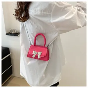 Detail of rose red mini crossbody bag with silver bow buckle worn by model