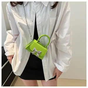 Detail of neon green mini crossbody bag featuring a silver metal bow and chain strap