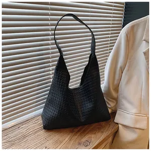 Close-up of black woven faux leather hobo bag on wooden surface with elegant light
