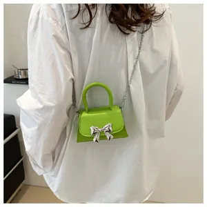 Neon green mini bag with silver bow detail shown worn by a model in a white shirt