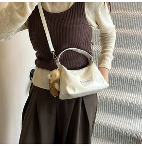 Detail of glossy beige crossbody bag with plush bear charm and adjustable strap