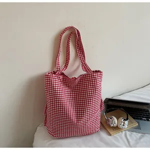 Detalle de bolso tote de lona a cuadros rojos junto a un portátil y unos auriculares