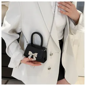 Close-up of black mini leather handbag featuring a silver metal bow and chain strap