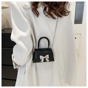 Detail of black mini crossbody bag with silver bow ornament and metallic chain strap