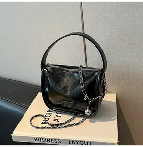 Detail of glossy black patent leather handbag featuring a silver chain and metal ball charm