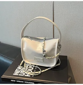 Detail of a creamy white patent leather crossbody bag with chain strap and Fashion plate