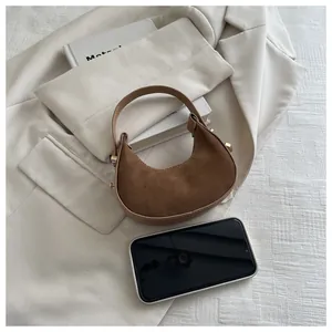 Detail of mini brown suede crescent bag with gold hardware and phone for size scale