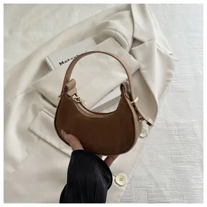 Detail of a brown suede half-moon bag featuring golden zipper and leather handle