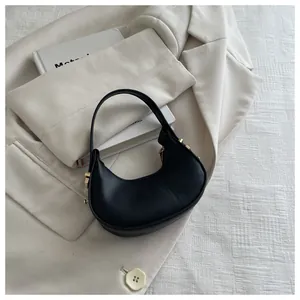 Detail of black faux leather moon bag with golden studs on a stylish blazer background