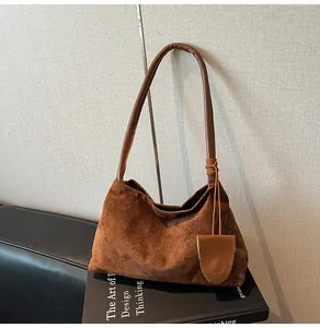 Détail du sac hobo en daim marron foncé avec bandoulière en cuir brillant sur livre