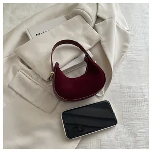 Detailed view of mini burgundy suede crescent handbag next to a smartphone for scale