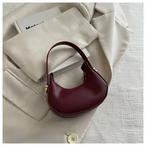 Detail of burgundy crescent handbag with golden zipper on white blazer background