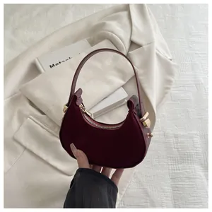 Close-up of a burgundy suede half-moon handbag with gold metal zipper and handle hardware