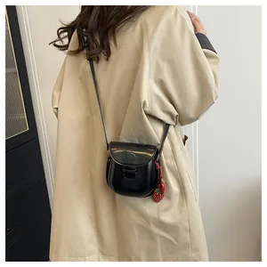 Detail einer schwarzen Lackleder-Satteltasche mit Erdbeer-Anhänger an einem Model