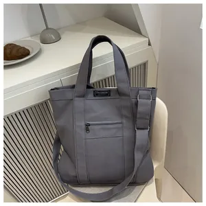 Donkergrijze canvas tote bag met verstelbare schouderriem en modelabel op het voorvak