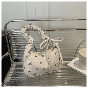 Close-up of white corduroy shoulder bag with black bow prints and ruffled strap detail