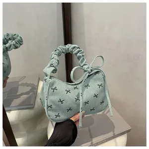 Detail of light green corduroy underarm bag with black bow prints and ruffled handle