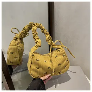Detail of mustard yellow corduroy underarm bag featuring black bow embroidery and ruched strap