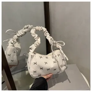 Close-up of white corduroy shoulder bag featuring black bow prints and ruffled cloud handle