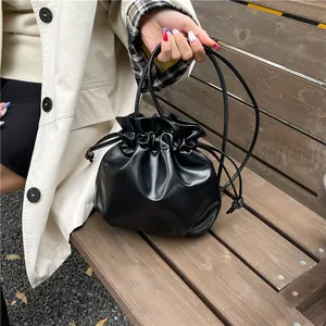 Black leather drawstring bucket bag with thin straps shown in an elegant outdoor setting