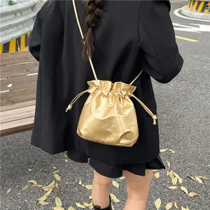 Metallic gold drawstring bucket bag in soft leather finish with long shoulder strap