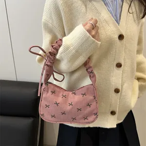 Pink corduroy underarm bag featuring black bow prints and a ruched handle design