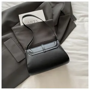 Chic black leather shoulder bag with flap closure placed on a grey blazer and book