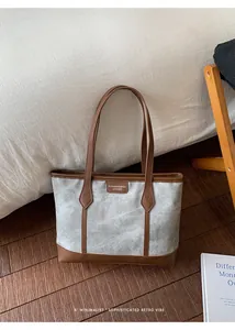 Detail view of large tote bag featuring grey canvas body and brown leather handles and trim