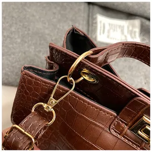 Détail de la texture cuir crocodile marron et des anneaux métalliques dorés du sac