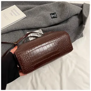 Détail de la texture cuir gaufré crocodile marron sur le sac bandoulière cylindrique