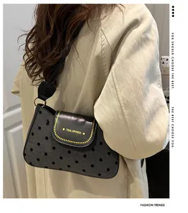 Detail of grey polka dot shoulder bag with black leather flap and yellow branding logo