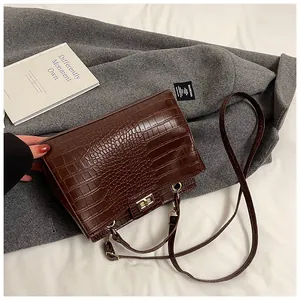 Détail du sac à main marron foncé à motif crocodile avec fermoir tournant doré sur manteau
