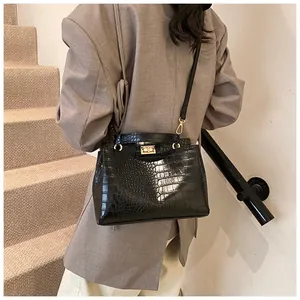 Détail d'un sac à main noir motif crocodile avec fermoir doré porté sur un blazer gris